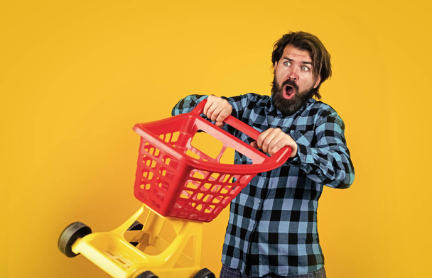 shopaholic concept. good discounts. bearded man in checkered shirt carry shopping cart. casual guy feel surprise about sales. surprised hipster with moustache in mall. male shopper - Photo, image