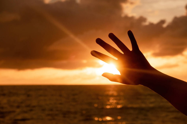 Mão levantada em silhueta sombra bloco sol dourado, cena principal é céu e mar. - Foto, Imagem