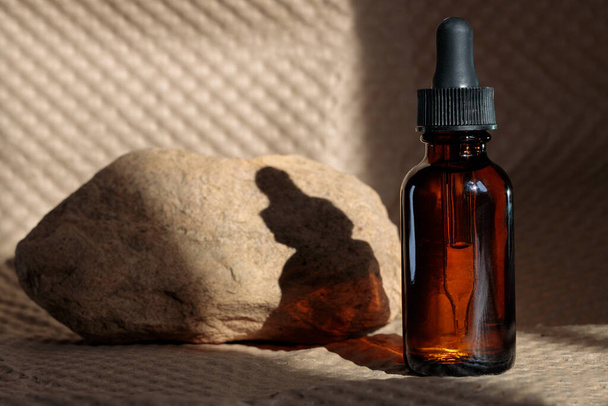 Skin care essential oil glass bottle with dropper and stone paper background. Moisturizing serum for facial skin. Aesthetics, minimalism. - Фото, зображення