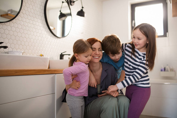 Mother of three little children hugging themr in bathroom at home. - Photo, image