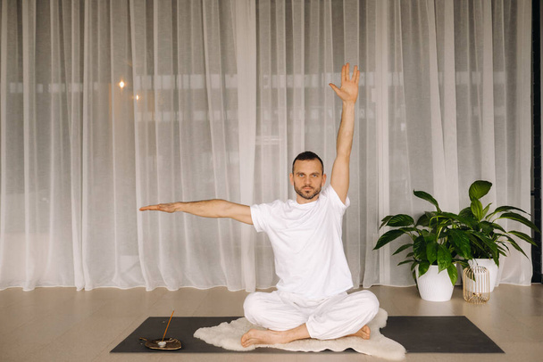 a man in white sportswear is doing yoga with a fitness room. the concept of a healthy lifestyle. - Valokuva, kuva
