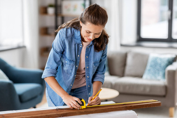 woman with ruler measuring wooden board at home - Foto, Bild