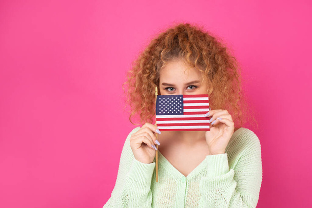 彼女の顔に笑顔の若い幸せな女の子は彼女の手にアメリカのフラグを保持しています.愛国心と自由の象徴. - 写真・画像