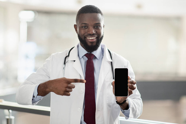 Handsome african american doctor pointing at smartphone, mockup - Foto, Bild