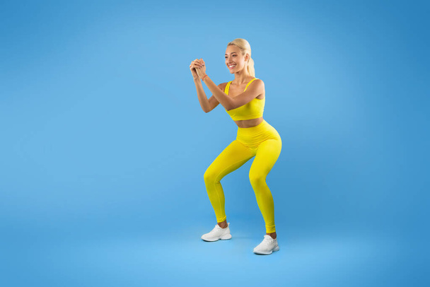 Uśmiechnięta młoda kobieta robi głębokie Squat ćwiczenia - Zdjęcie, obraz