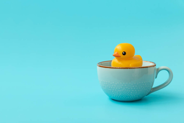 Yellow rubber duck swimming into cup of tea on blue background. Creative summer vacation concept - Photo, image