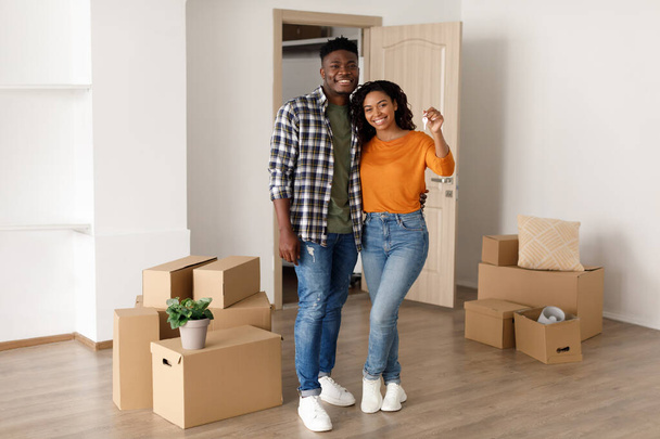 Heureux couple afro-américain tenant une nouvelle maison clé debout à l'intérieur - Photo, image