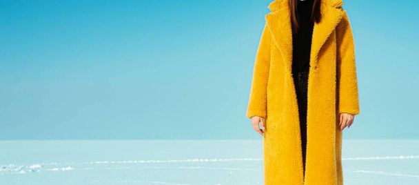 Young running woman in yellow coat walking on snowy ice.  - Фото, изображение