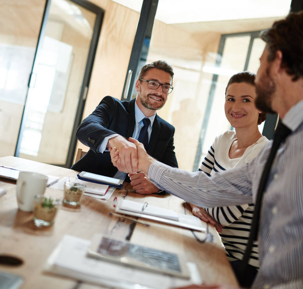 Deals im Sitzungssaal. Aufnahme von zwei Geschäftsleuten beim Händeschütteln in einem Büro, während ein Kollege zusieht. - Foto, Bild