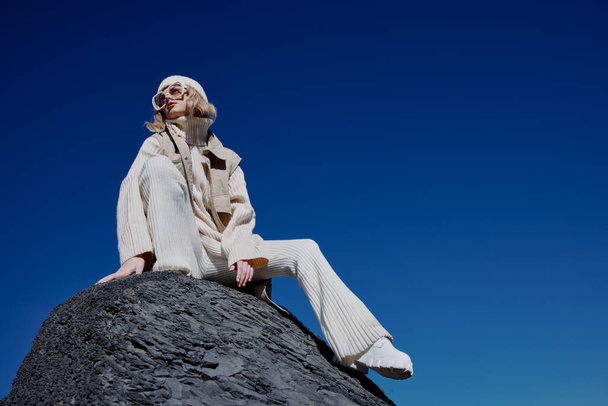 mujer joven en ropa de otoño se encuentra en un paisaje de roca azul cielo paisaje - Foto, Imagen