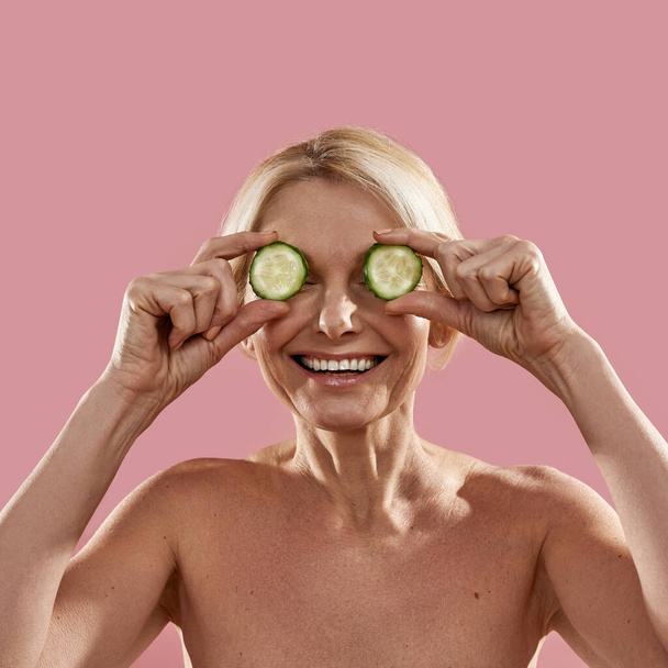 Mature woman covering eyes with cucumber slices - Fotó, kép