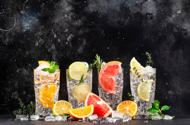 Set de cócteles Gin tonic y cítricos. Bebidas alcohólicas con lima, limón, pomelo, naranja, soda y hierbas en vasos de tubo, fondo contador de bar negro. Cóctel de verano - Foto, Imagen
