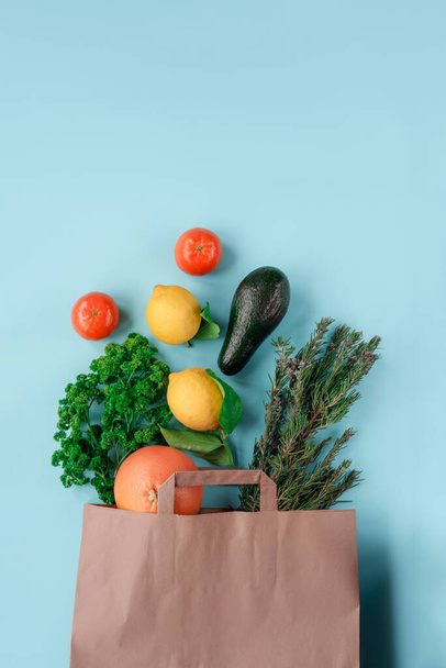 Grapefruit, lemon, avocado, tangerines, rosemary and parsley in paper bag on blue background. Top view, flat lay - Fotoğraf, Görsel