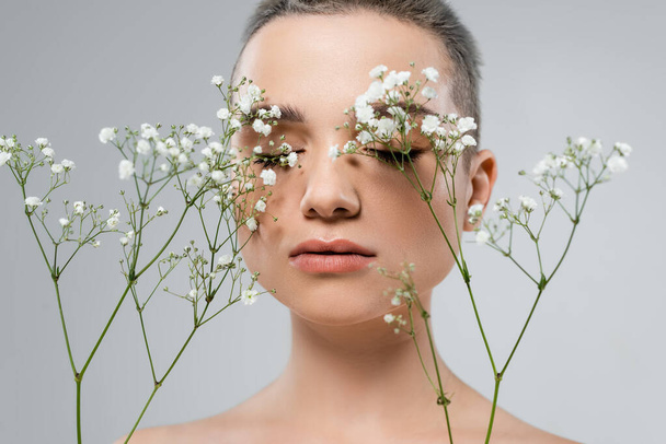 portrait of charming woman with perfect skin near branches of gypsophila isolated on grey - Fotó, kép