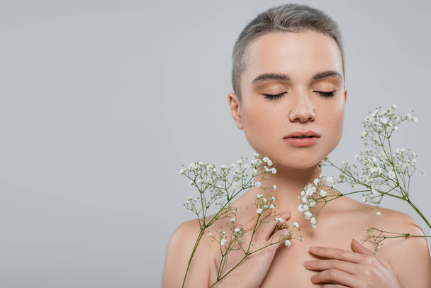 charming woman with closed eyes and naked shoulders near branches of gypsophila isolated on grey - Фото, изображение