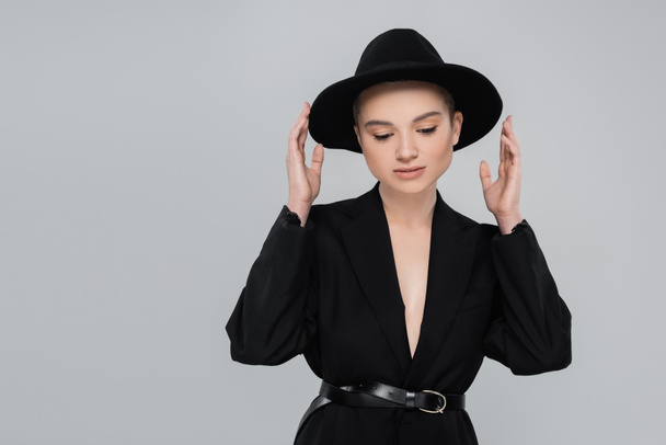 trendy woman with natural makeup touching black brim hat isolated on grey - Foto, Imagem