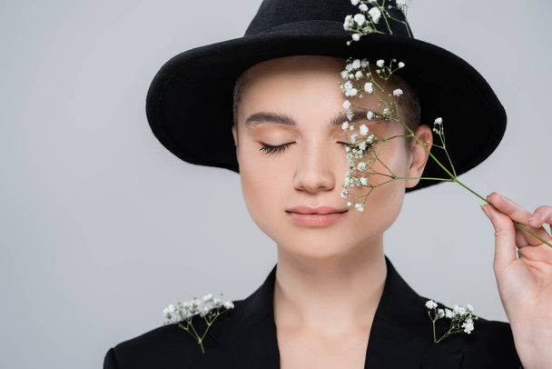 charming woman with closed eyes holding branch of gypsophila near perfect face isolated on grey - Photo, Image