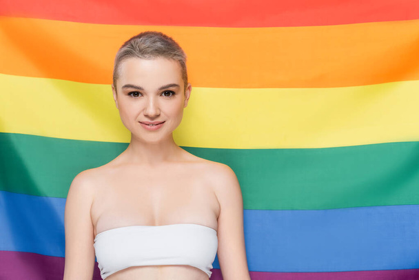 young woman in white top looking at camera near lgbt flag on background - Photo, Image