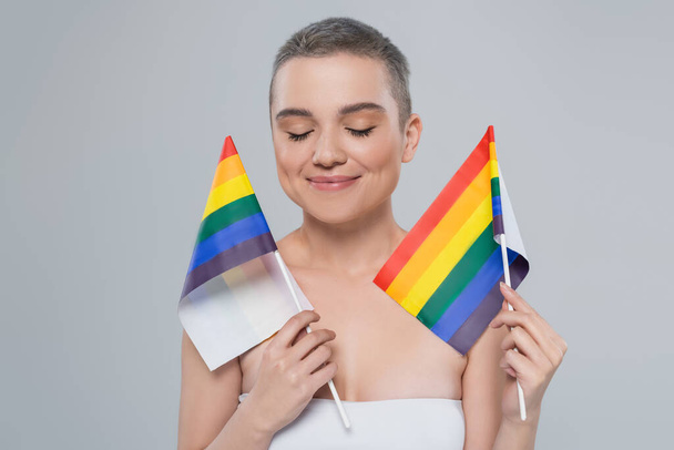 smiling woman with closed eyes holding small lgbt flags isolated on grey - Foto, imagen