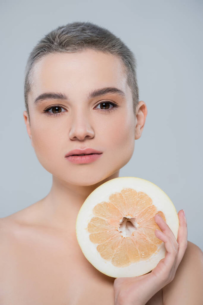 portrait of pretty woman with short hair looking at camera near half of grapefruit isolated on grey - Фото, зображення