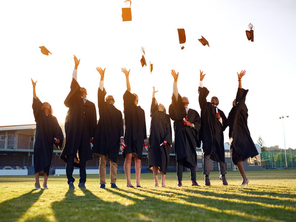 Έφτασαν στο τέλος των ακαδημαϊκών τους χρόνων. Πυροβολισμός ομάδας φοιτητών που πετούν τα καπέλα τους στον αέρα την ημέρα της αποφοίτησης. - Φωτογραφία, εικόνα