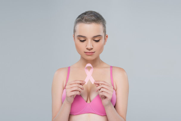 young woman with short hair holding breast cancer awareness ribbon isolated on grey - Fotoğraf, Görsel