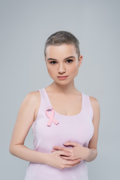 młoda kobieta z wstążką świadomości raka piersi na szczycie zbiornika patrząc na kamerę odizolowaną na szaro - Zdjęcie, obraz