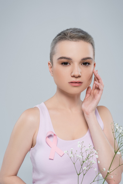 красивая женщина с раком молочной железы осведомленность лента на цистерне и белые крошечные цветы изолированы на серый - Фото, изображение
