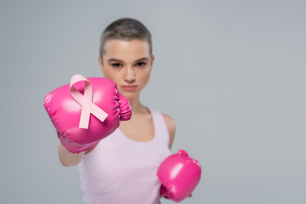 young woman with pink awareness ribbon on boxing glove on blurred background isolated on grey - Photo, Image