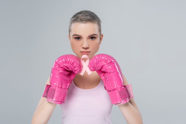 jovem mulher em luvas de boxe rosa segurando fita consciência câncer de mama isolado em cinza - Foto, Imagem