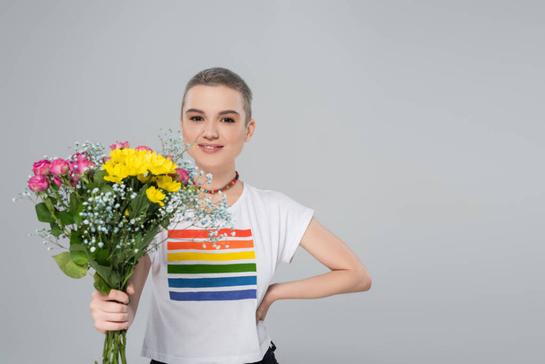 happy woman in lgbt colors t-shirt holding flowers isolated on grey - Фото, изображение