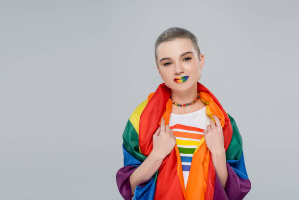 young and pretty woman with lgbt flag on shoulders looking at camera isolated on grey - Foto, Imagen