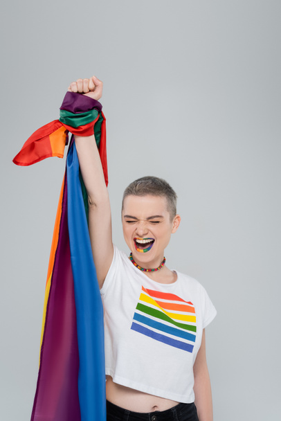 excited woman holding lgbt flag with raised hand isolated on grey - Foto, afbeelding