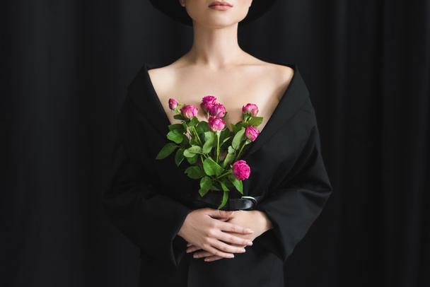 visão parcial da jovem com pele perfeita posando com rosas rosa no fundo preto - Foto, Imagem