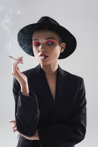 woman in black fedora hat and blazer smoking isolated on grey - Fotoğraf, Görsel