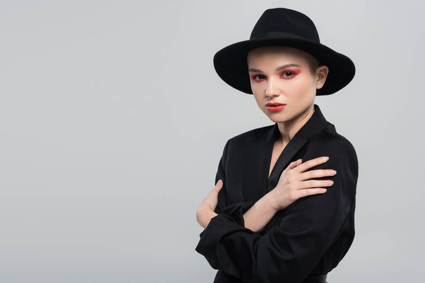 woman in black blazer and brim hat posing with crossed arms isolated on grey - Фото, зображення