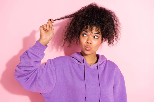 Photo of dreamy doubtful lady dressed purple hoodie lips pouted hand arm hair curl looking empty space isolated pink color background - Foto, Imagem