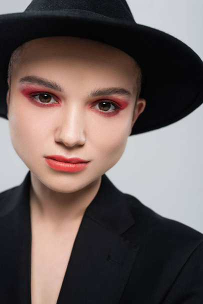 portrait de jeune femme au maquillage rouge carmin, coiffée d'un chapeau fedora noir isolé sur fond gris - Photo, image