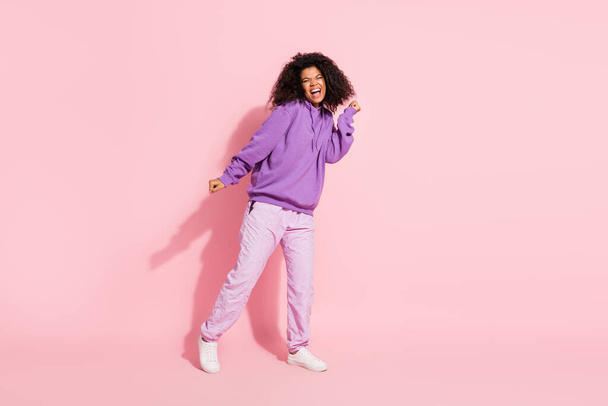 Photo of shiny lucky afro girl wear violet sweatshirt dancing empty space rising fist smiling isolated pink color background - Valokuva, kuva