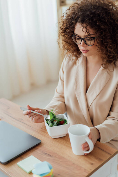 Kobieta jeść zdrowe zielone jedzenie w biurze w pobliżu notatnika - Zdjęcie, obraz