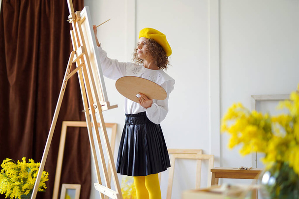 Cute little girl artist in yellow beret painting a still life of flowers while holds color pallete  - Foto, Bild