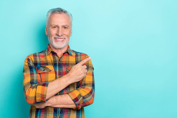 Photo of cheerful man pensioner dressed checkered shirt pointing empty space isolated teal color background - Fotó, kép