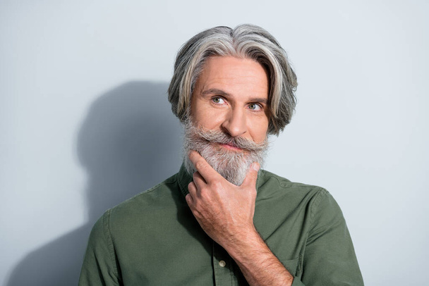 Portrait of attractive well-groomed bewildered grey-haired man touching beard making decision isolated over gray pastel color background - Photo, image