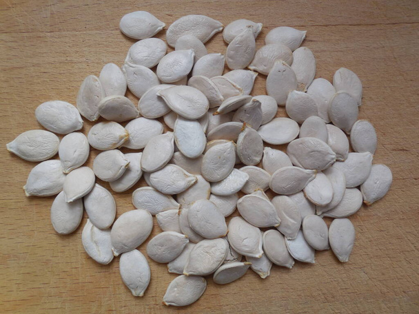 Large white seeds (fruits) of pumpkin (cucurbita) are scattered on a wooden board. - Fotoğraf, Görsel