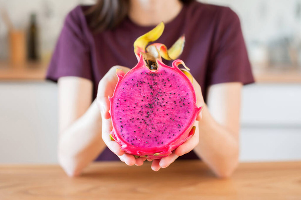 Tyttö pitää käsissään leikattu lohikäärme hedelmä pitahaya kotona keittiössä lähikuva. pehmeä fokus - Valokuva, kuva