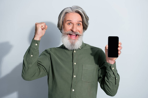 Retrato de hombre de pelo gris alegre guapo dispositivo de celebración gadget regocijo aislado sobre fondo de color pastel gris - Foto, imagen