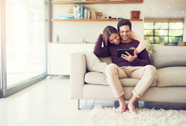 Estamos pegados como pegamento. Foto de una alegre pareja joven usando una tableta digital mientras se relaja en el sofá en casa. - Foto, Imagen