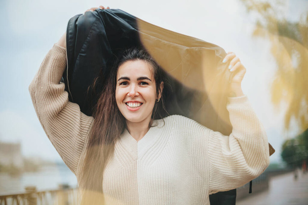 Молода щаслива весела жінка під дощем в шторм в осінній день стоячи на міській вулиці, позитивна жінка покриває голову пальто і посміхається на камеру Концепція щастя
 - Фото, зображення
