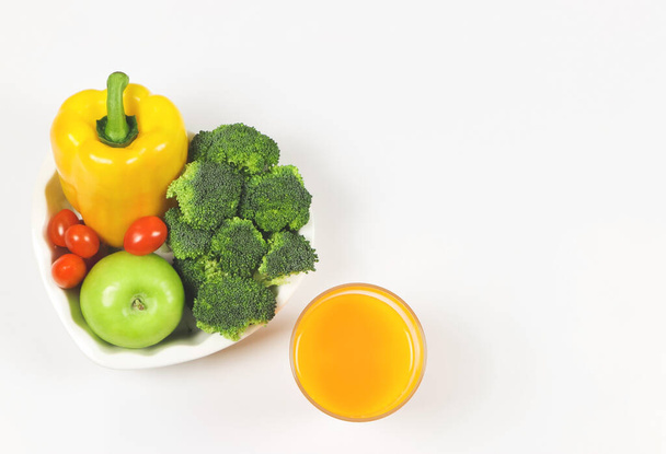 Κάτοψη ή επίπεδη lay λαχανικά Capsicum, ντομάτες μπρόκολο και πράσινο μήλο σε σχήμα καρδιάς πλάκα σε λευκό φόντο με ένα ποτήρι χυμό πορτοκαλιού, αντίγραφο χώρο, υγιεινό τρόπο ζωής και την έννοια της απώλειας βάρους. - Φωτογραφία, εικόνα