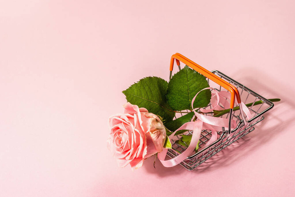 Sale concept with a shopping basket and fresh rose. Zero-waste, trendy hard light, dark shadow, flat lay. Women, Valentine's or Mother's Day, Wedding. Delicate pink background, copy space - Φωτογραφία, εικόνα